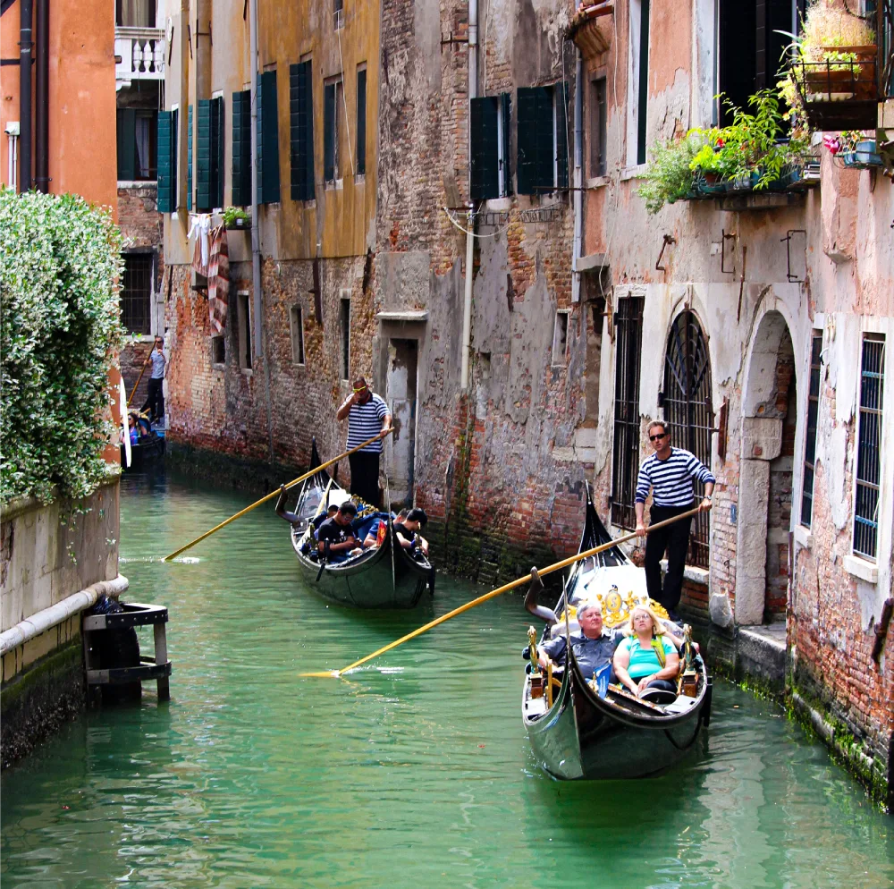 Gondolas gliding through a narrow canal in Venice with historic buildings on both sides